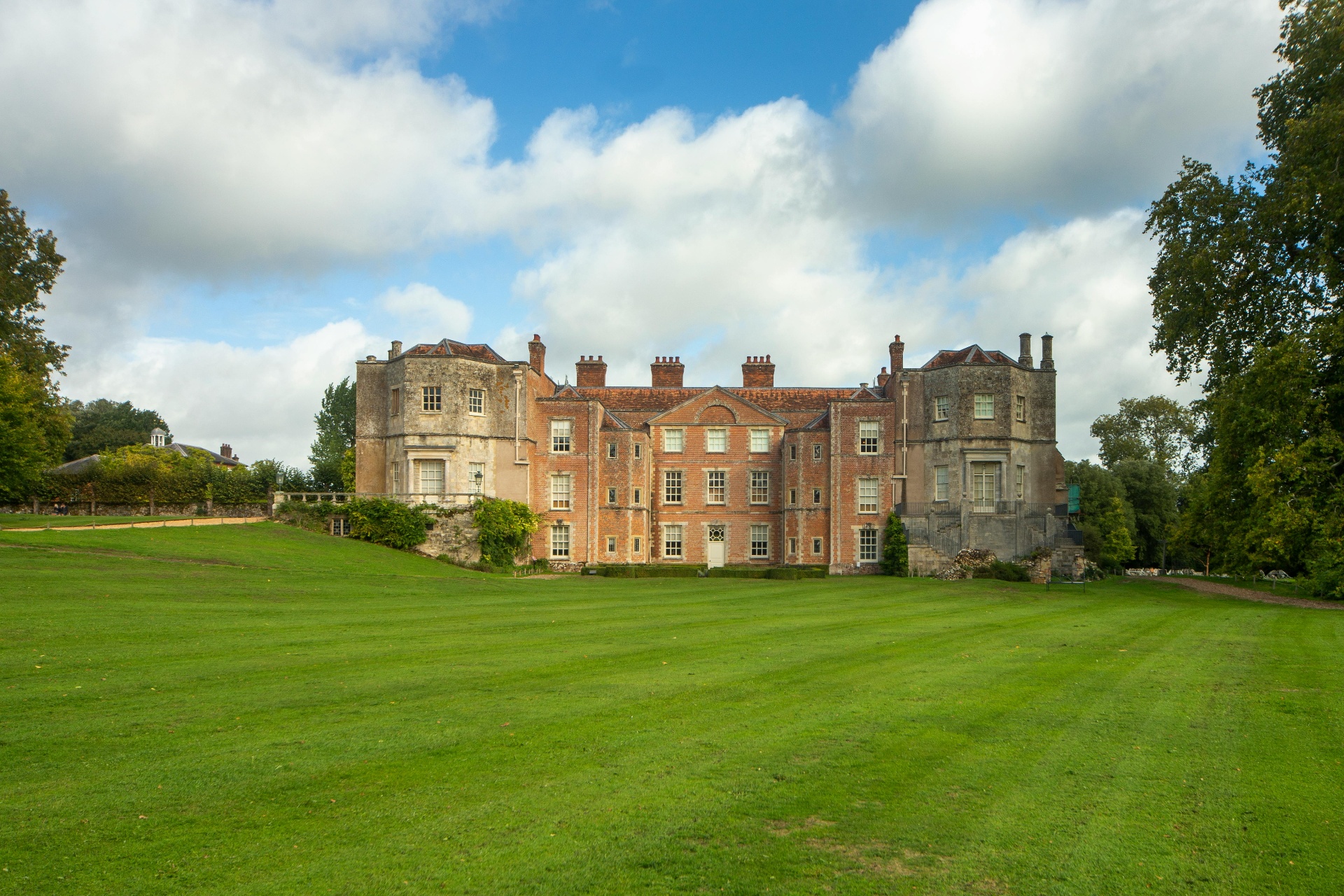 A stately English manor at golden hour, framed by lawns and ancient trees